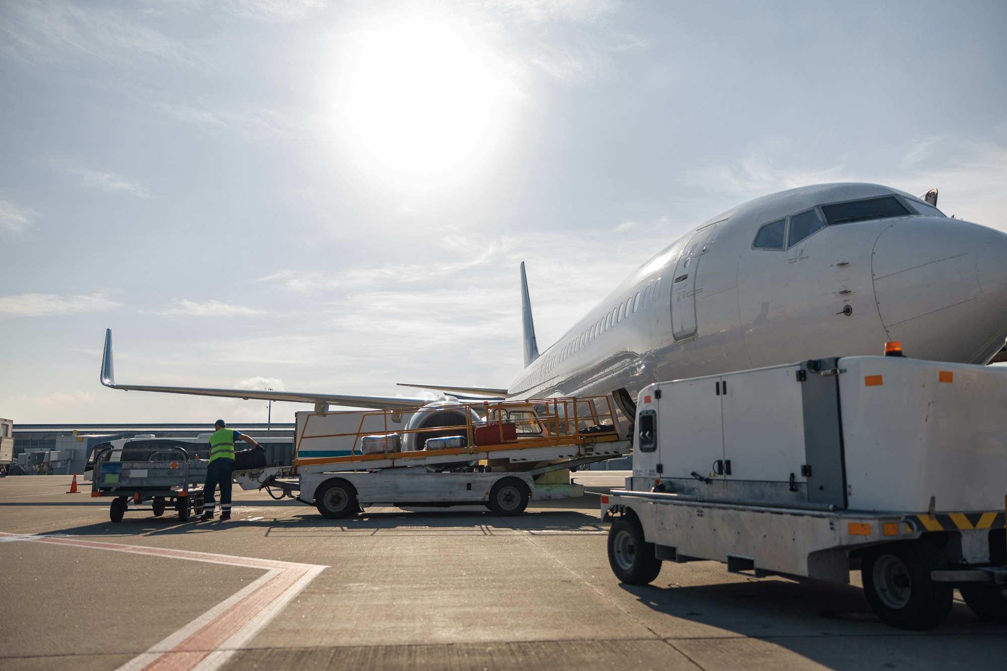 Worker loading baggage on conveyor belt to an airplane outdoors on a daytime